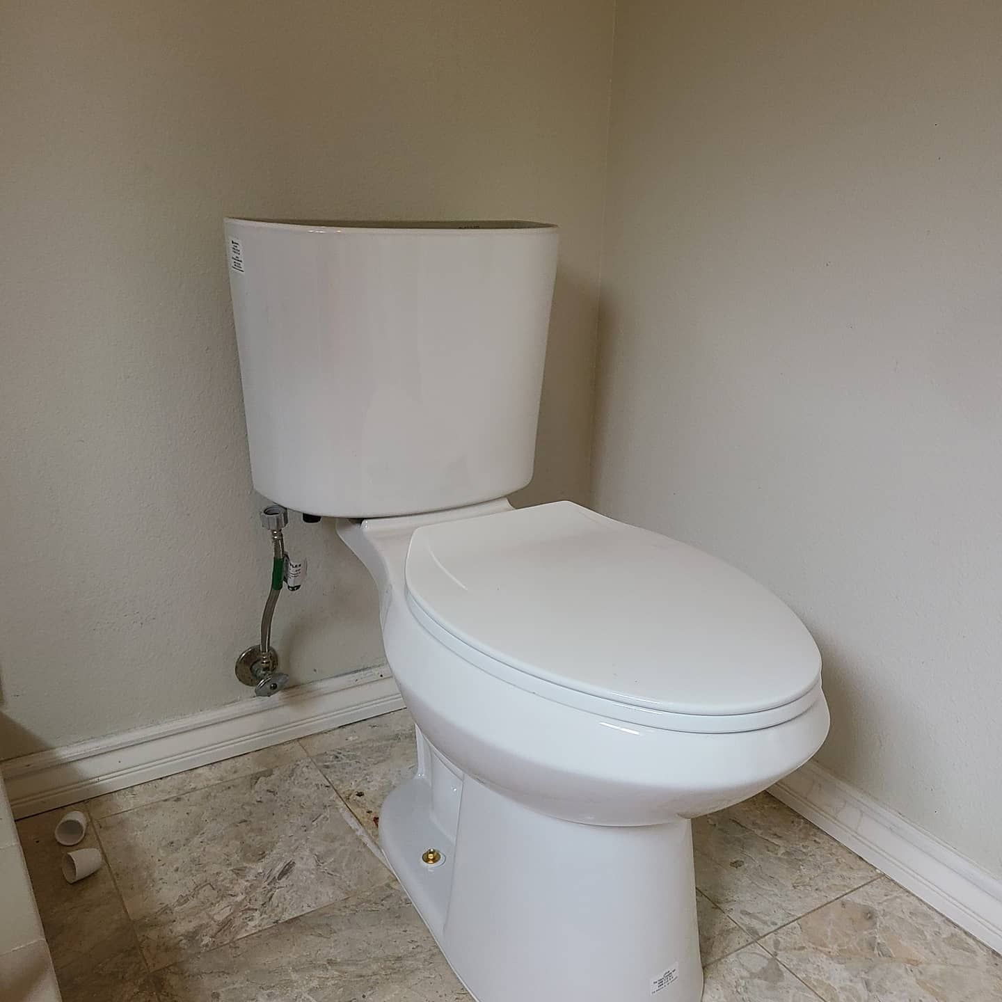 White toilet in a bathroom with beige tile flooring and light gray walls.