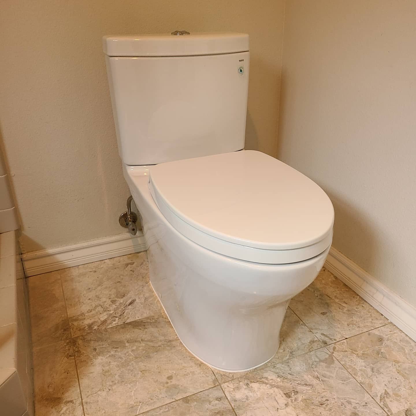 White toilet in a bathroom, with a closed lid. Beige tiled floor, light walls.