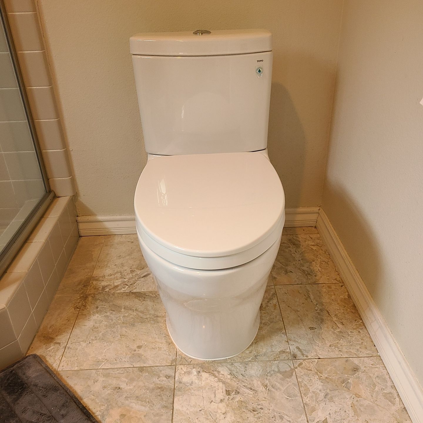 White, two-piece toilet in a bathroom with beige tile and walls.