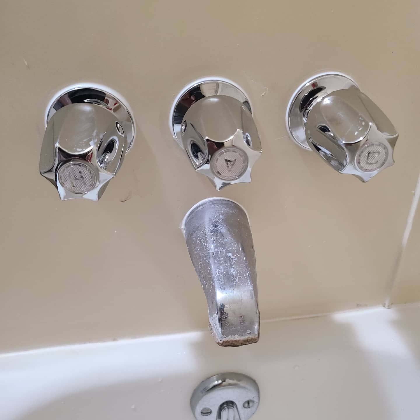Bathtub fixtures: three chrome faucet handles and spout on a beige wall.