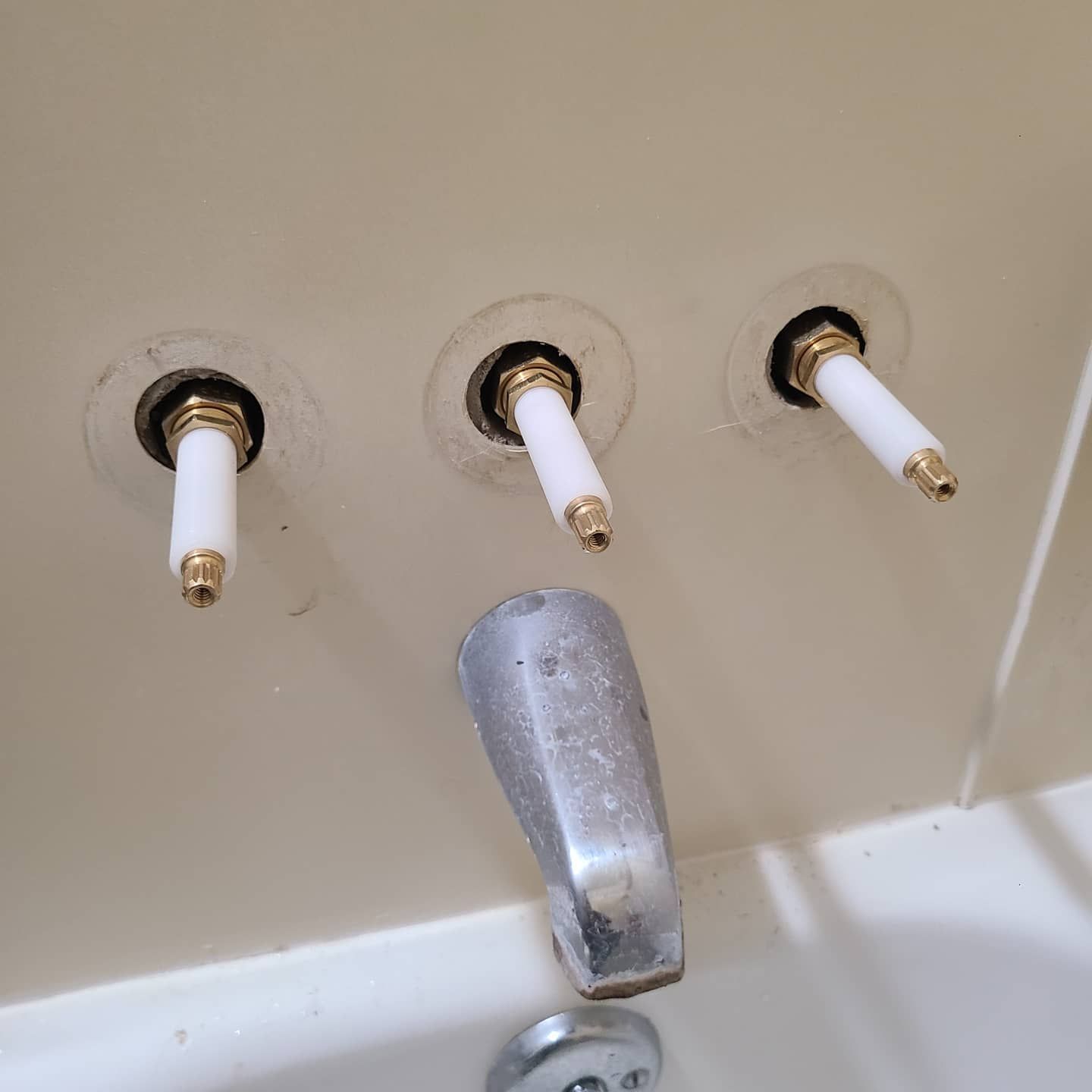 Three faucet stems and a spout in a bathtub.