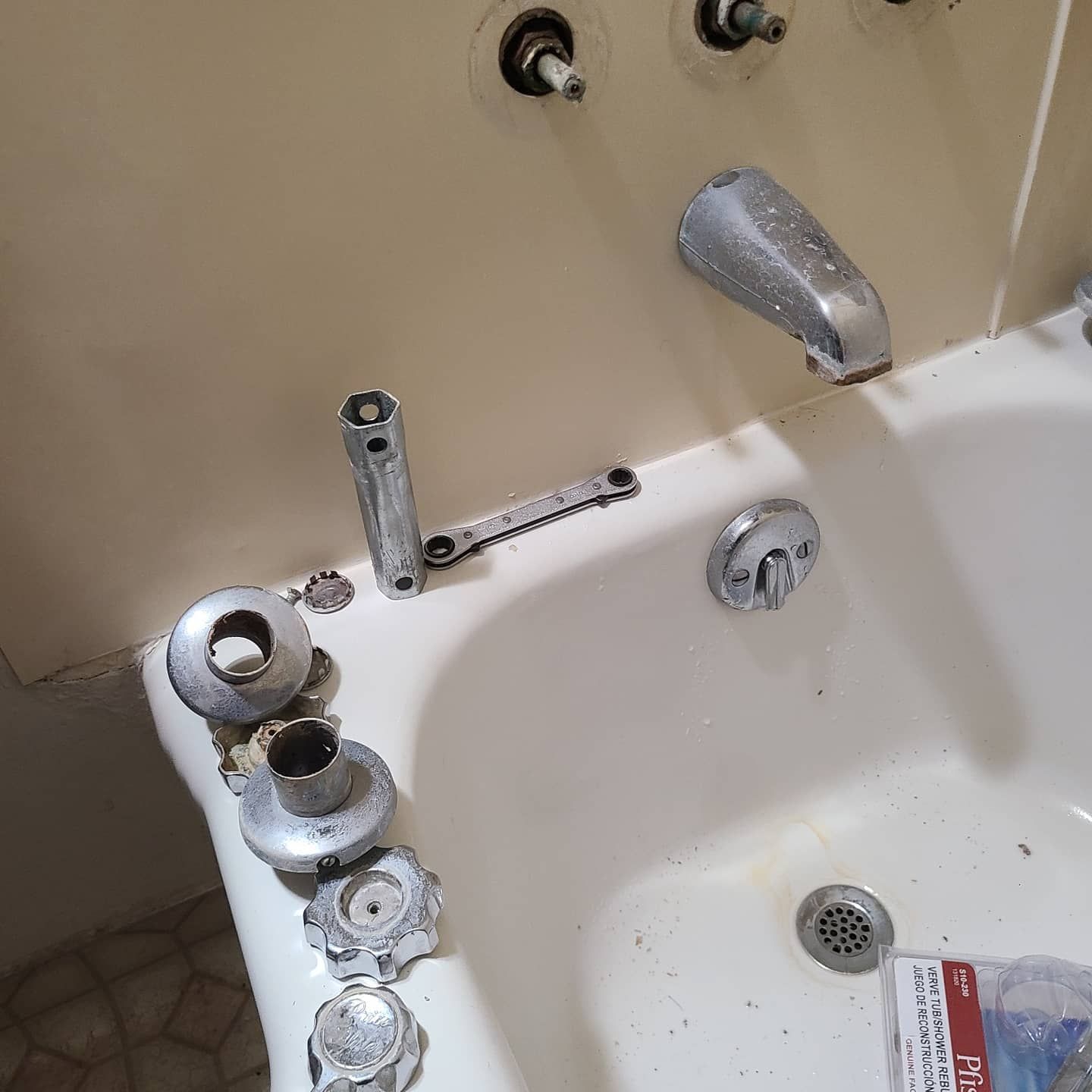Bathtub fixture parts laid out on a tub. Chrome faucets are missing handles, some components are in the tub.
