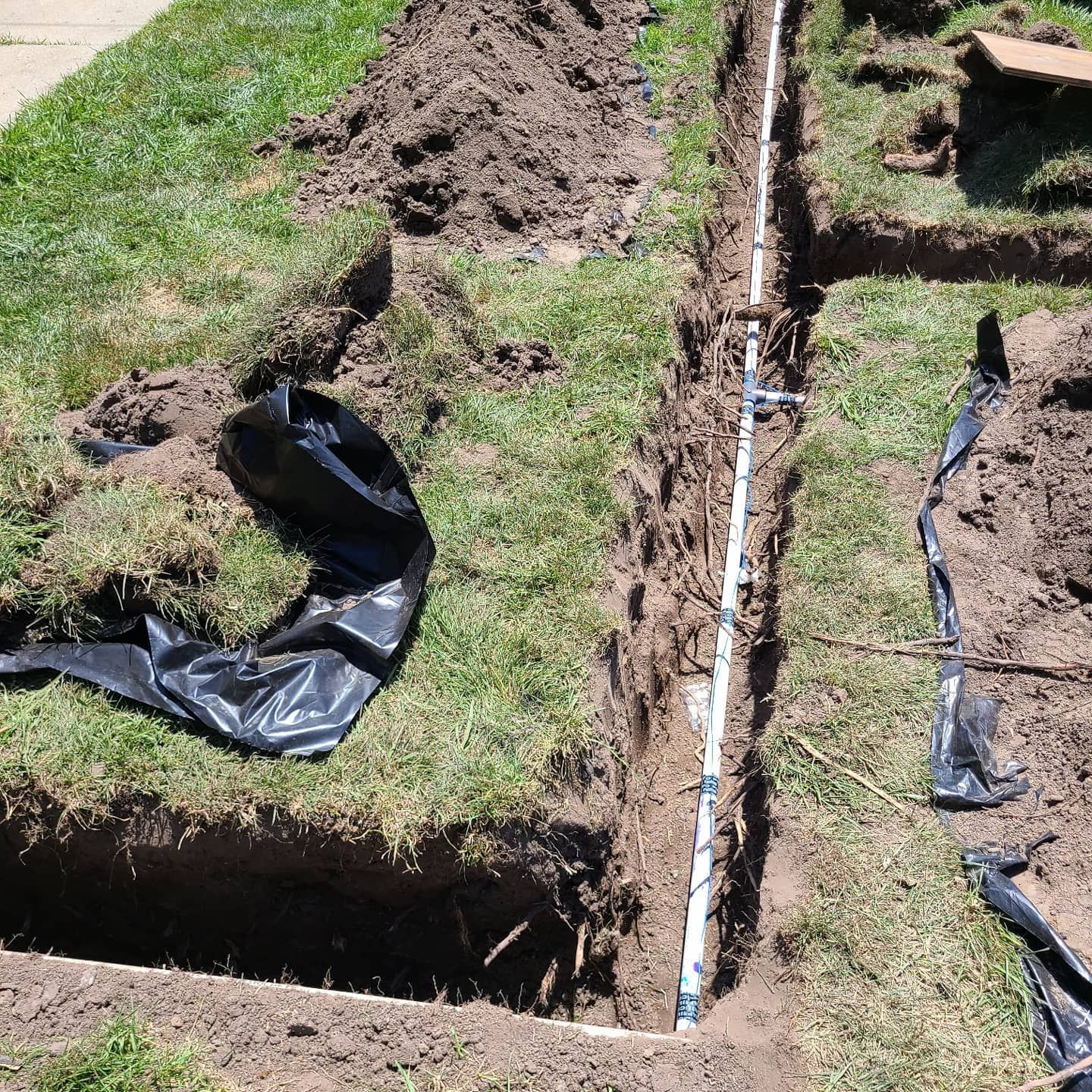 A trench in a grassy yard with white PVC pipe for irrigation installed and covered in dirt.