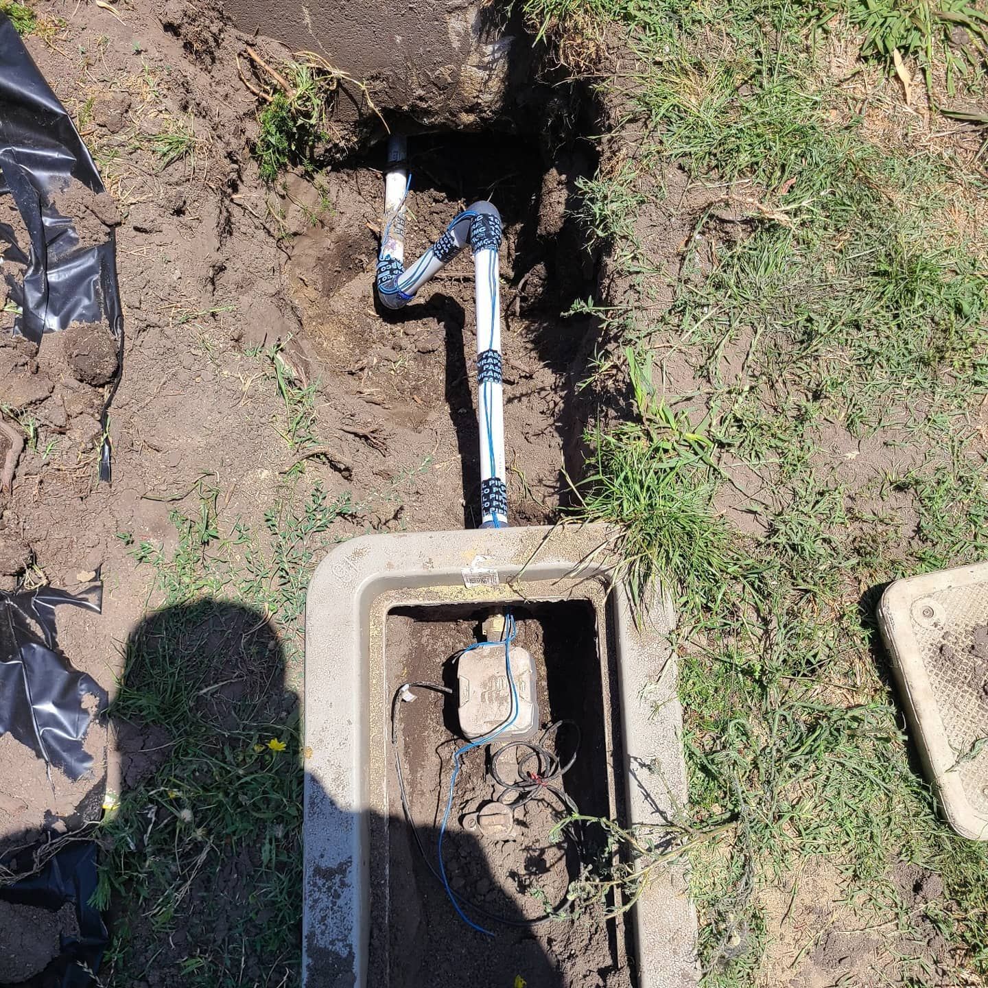 Open irrigation valve box with exposed pipes, soil, and grass.
