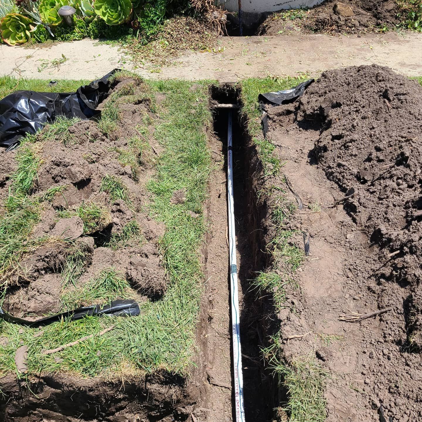 Trench in grassy yard with white pipe running through it, likely for utilities.
