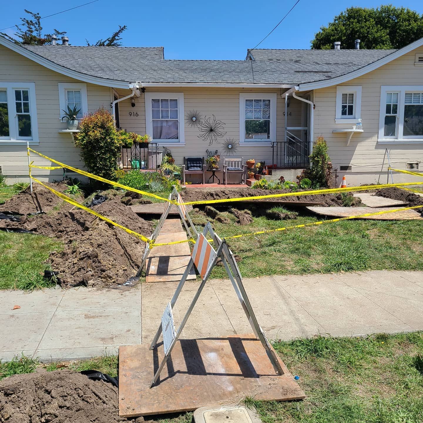 Yellow house with front yard under construction, caution tape, dirt piles, and construction sign.