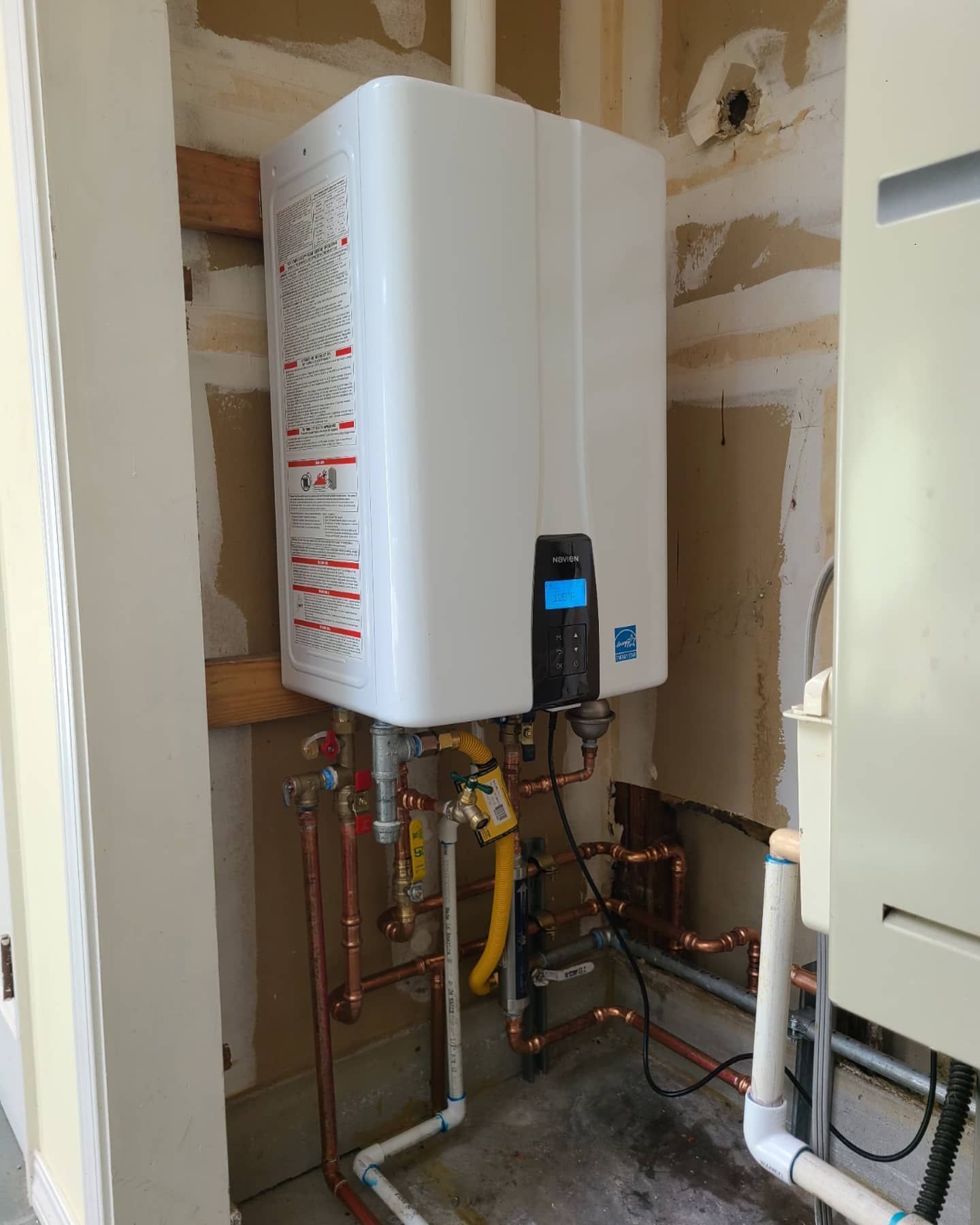 A white tankless water heater with copper pipes in a utility closet.