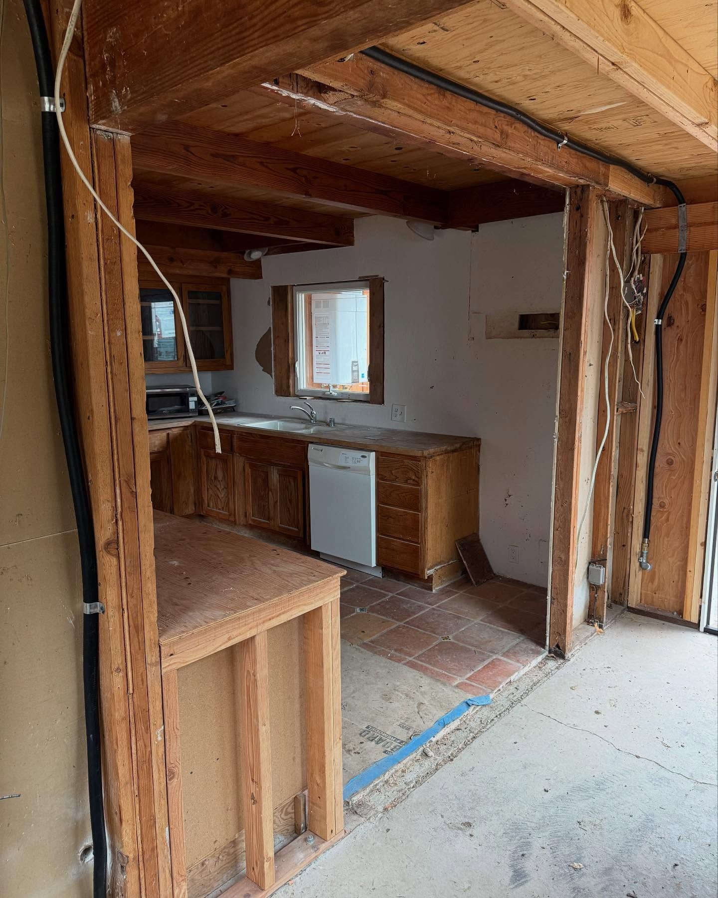 Kitchen undergoing renovation; exposed beams and studs, cabinets, appliances visible.