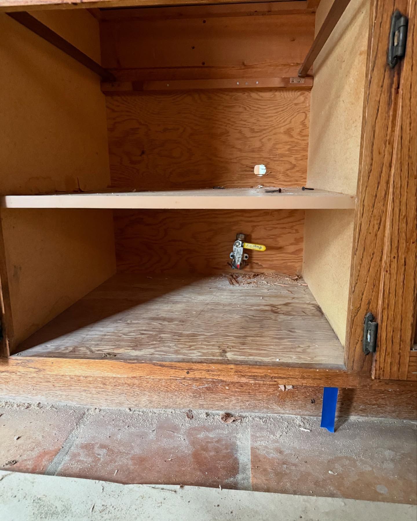 Inside of a wooden cabinet with a shelf and a gas valve. The floor has debris.
