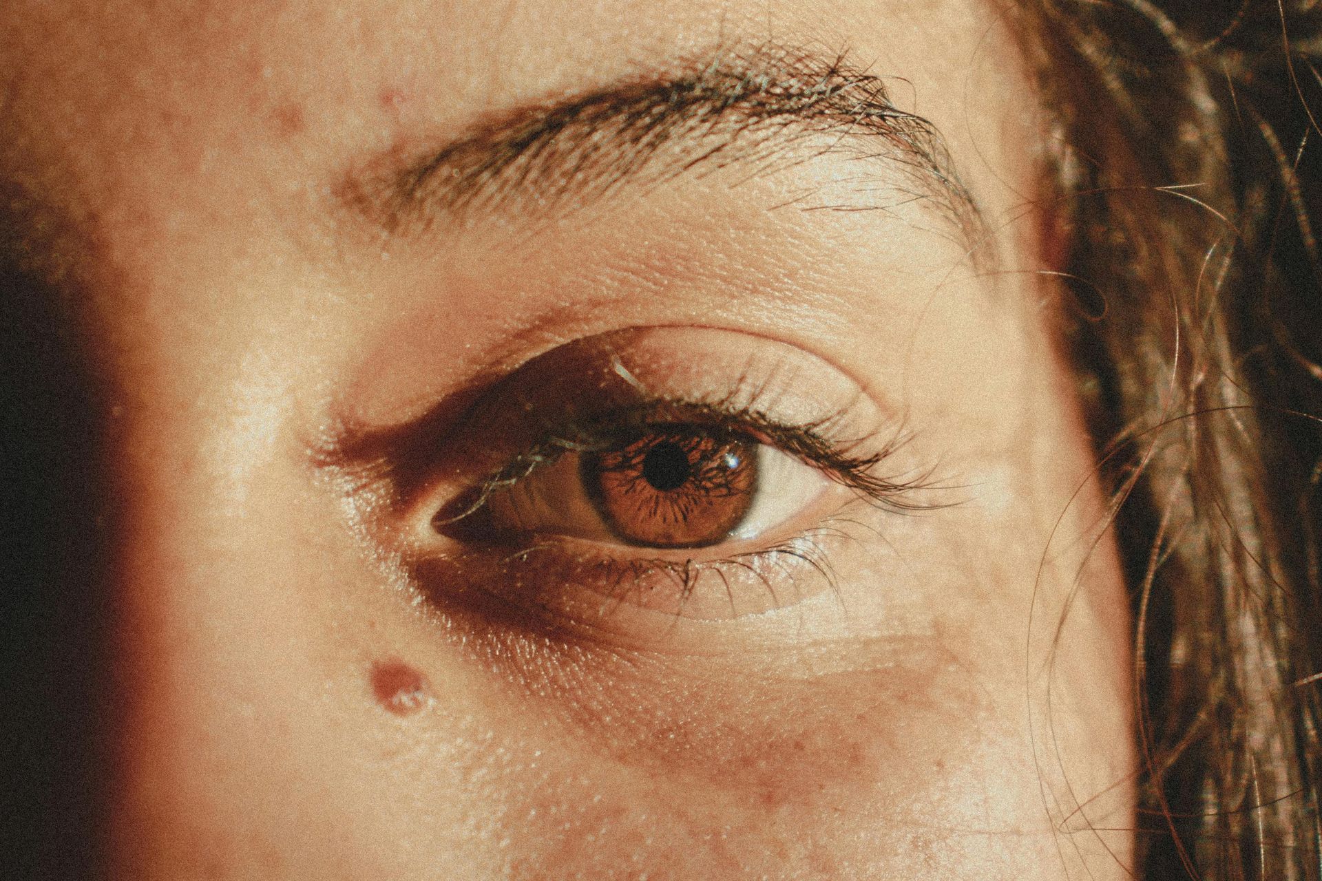 A close up of a woman 's brown eye with a spot on her forehead.