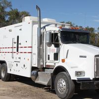 A white kenworth truck is parked in the dirt with ELI on the side door