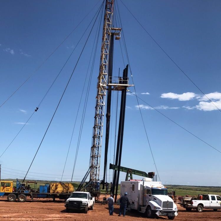 A white truck is parked in front of a large drilling rig