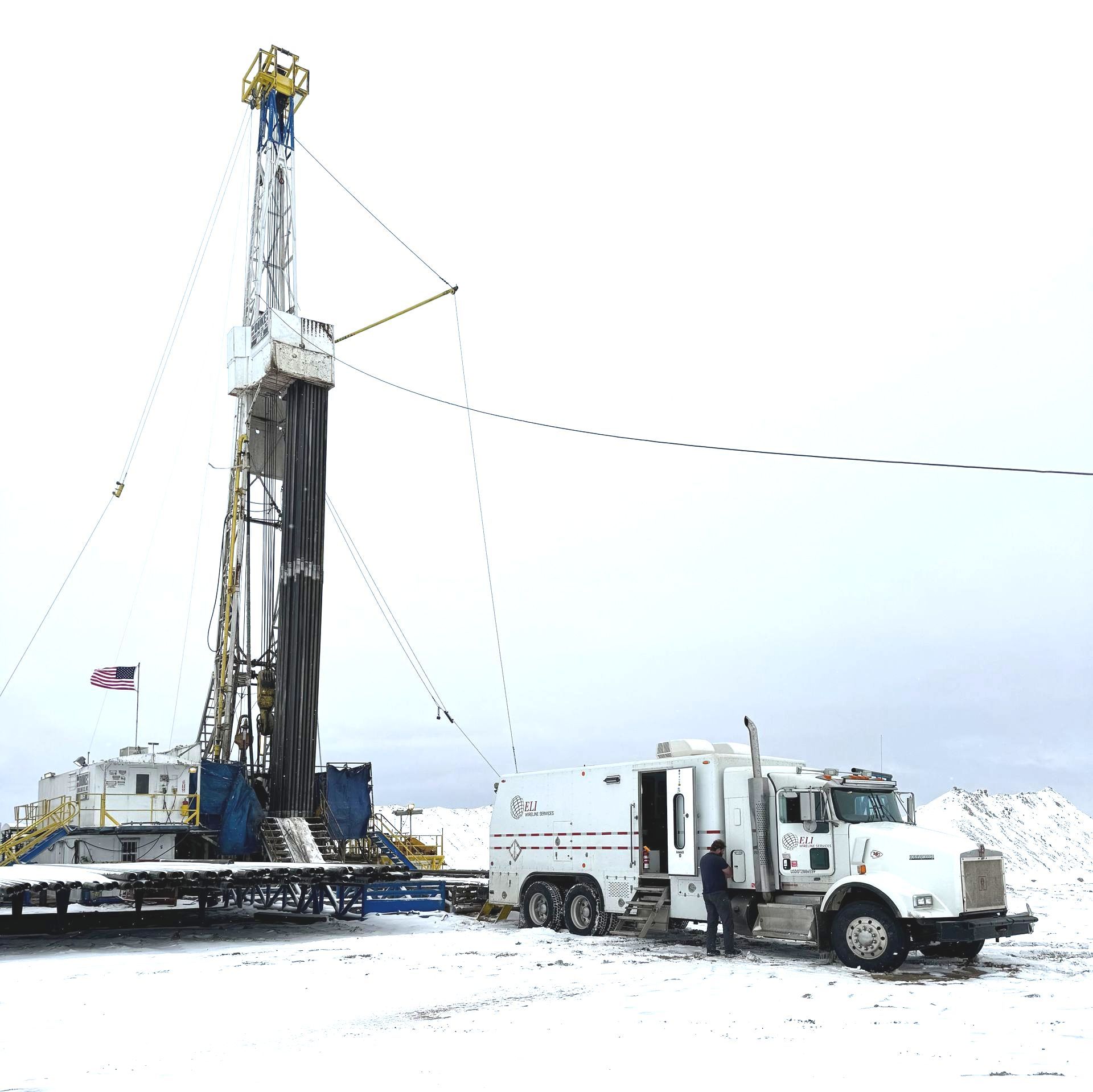 A truck is parked next to a drilling rig in the snow.