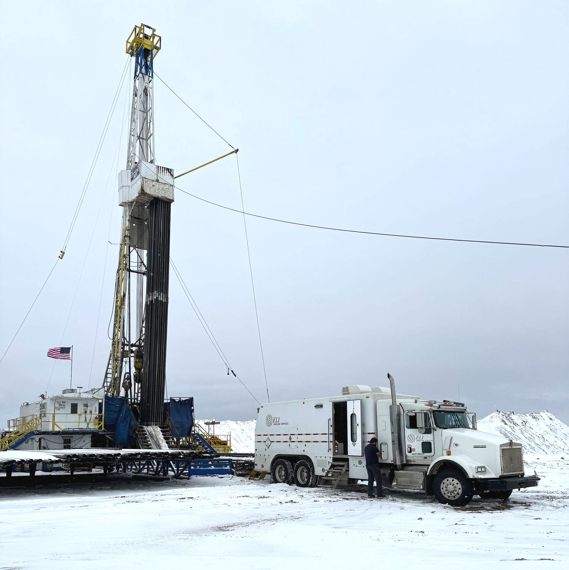 A truck is parked in front of a drilling rig in the snow