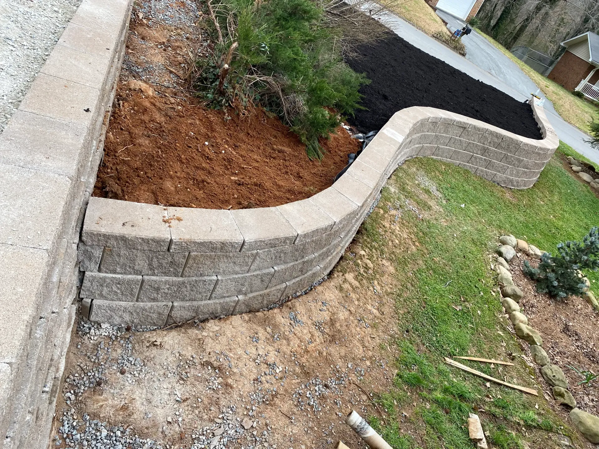 Stone retaining wall with curved edges; mulch and plants in the bed.