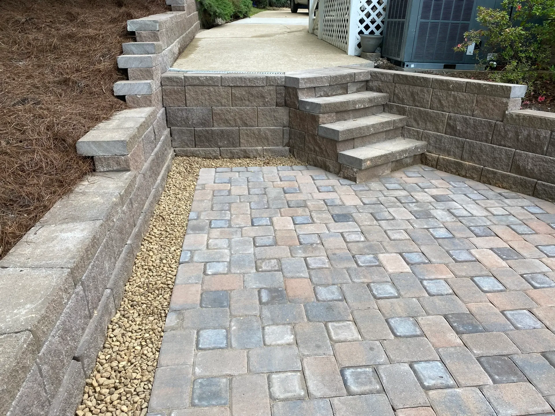 Brick patio with stone walls and stairs leading to a gravel path and elevated yard.