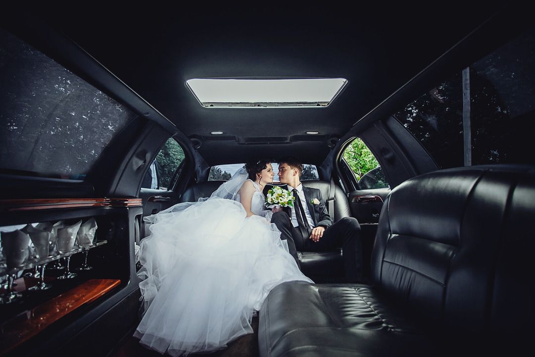 A bride and groom are sitting in the back seat of a limousine.