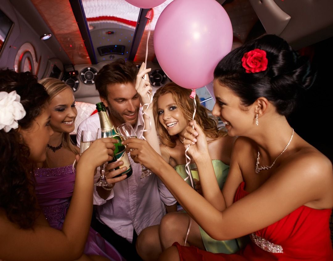 A group of people toasting in a limousine with pink balloons