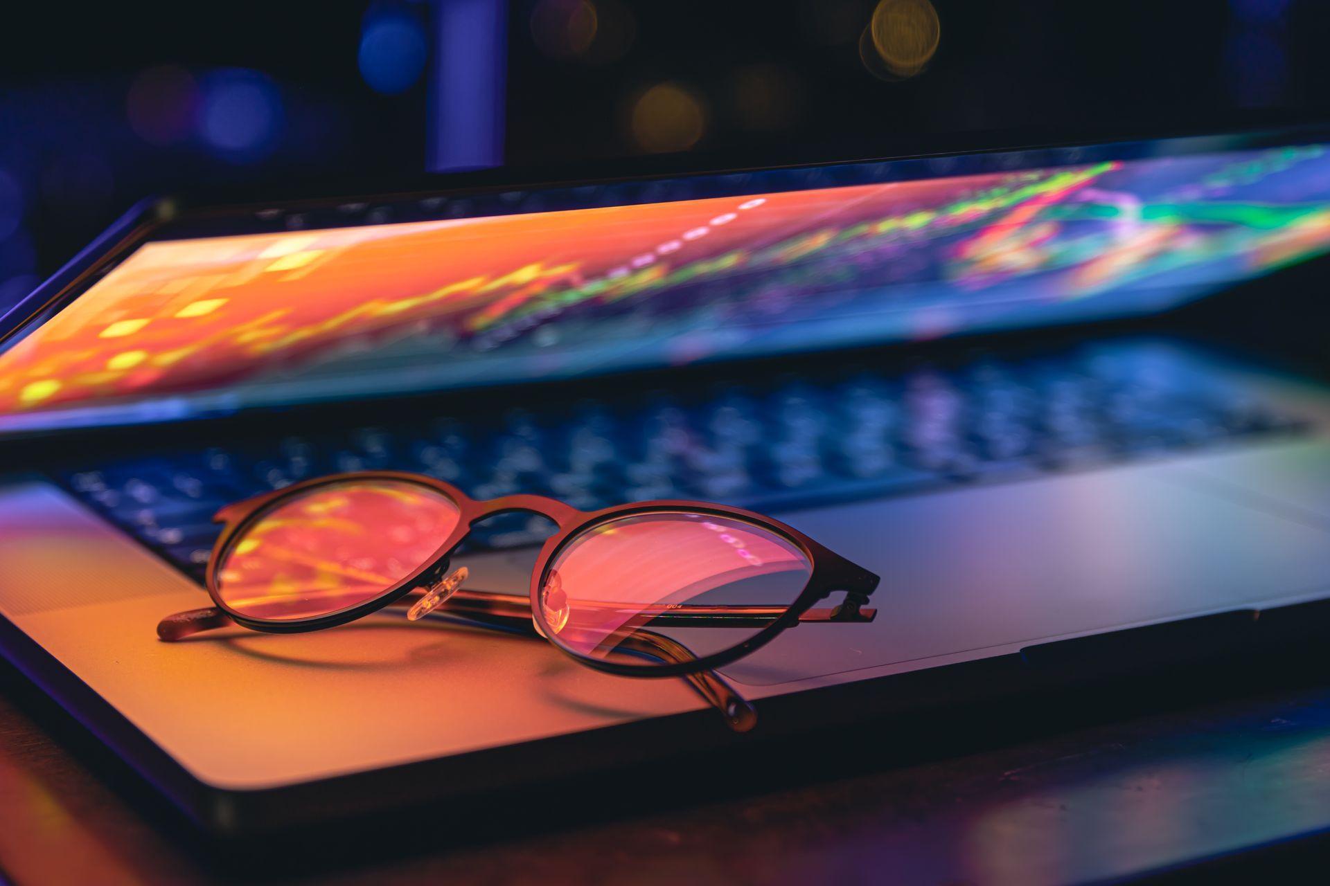 Lunettes posées sur un ordinateur dans une ambiance tamisée.