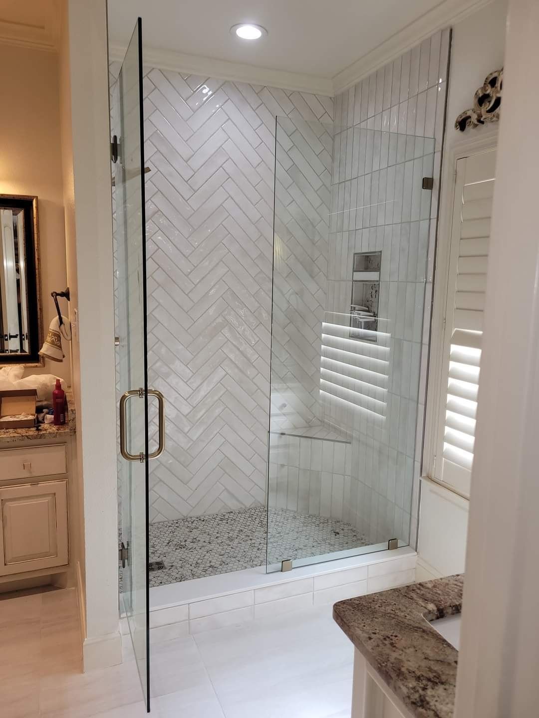 A bathroom with a walk in shower and a herringbone tile wall.