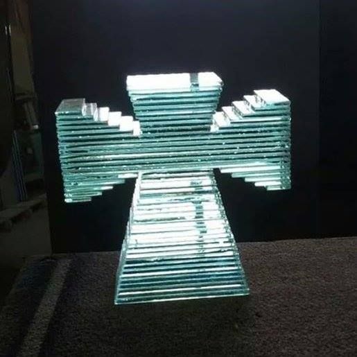 A glass cross is sitting on a table in front of a black wall