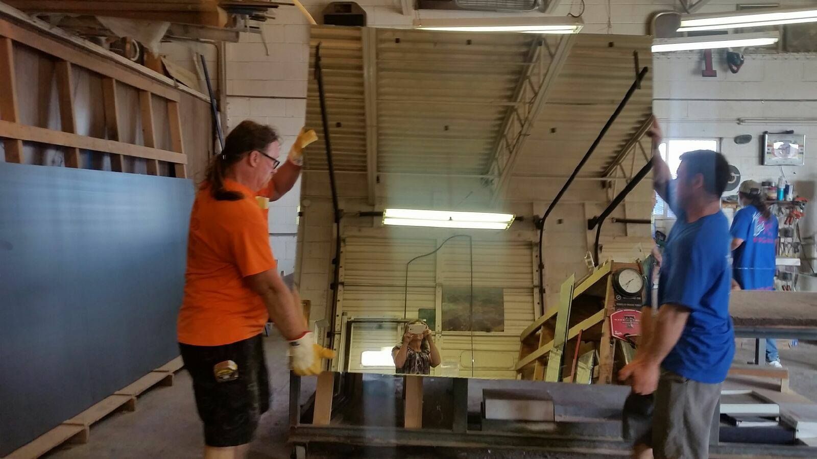 Two men are working on a large mirror in a factory.