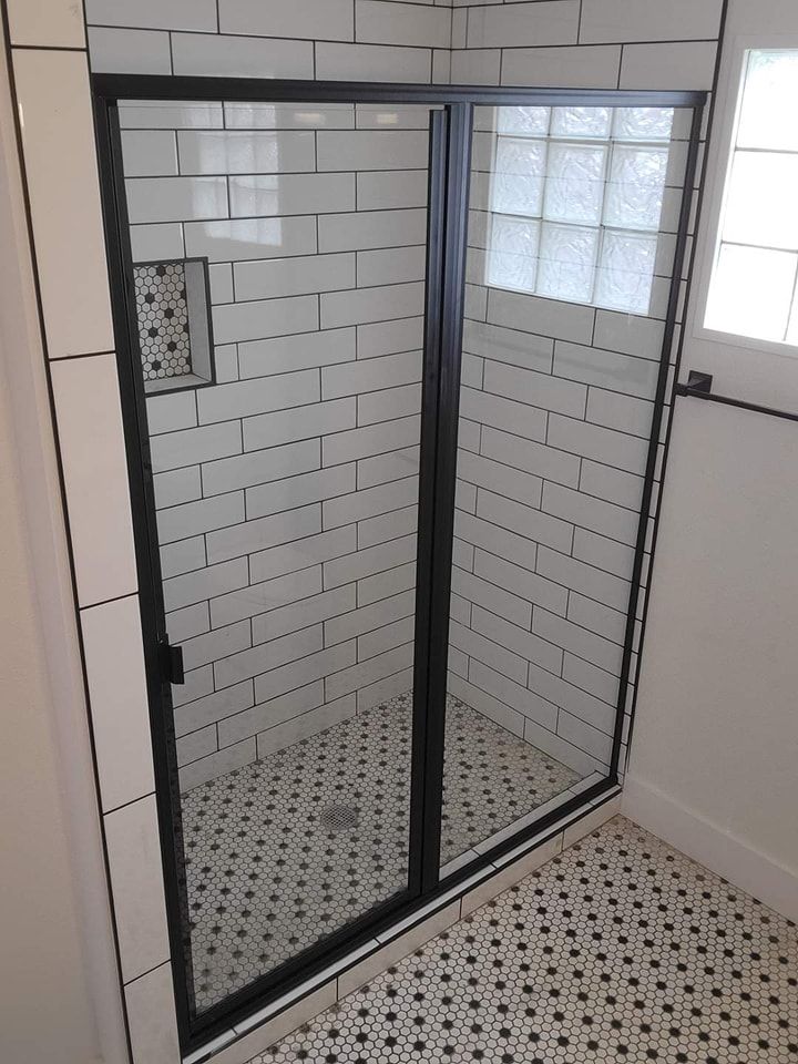 A bathroom with white tiles and a black shower door.