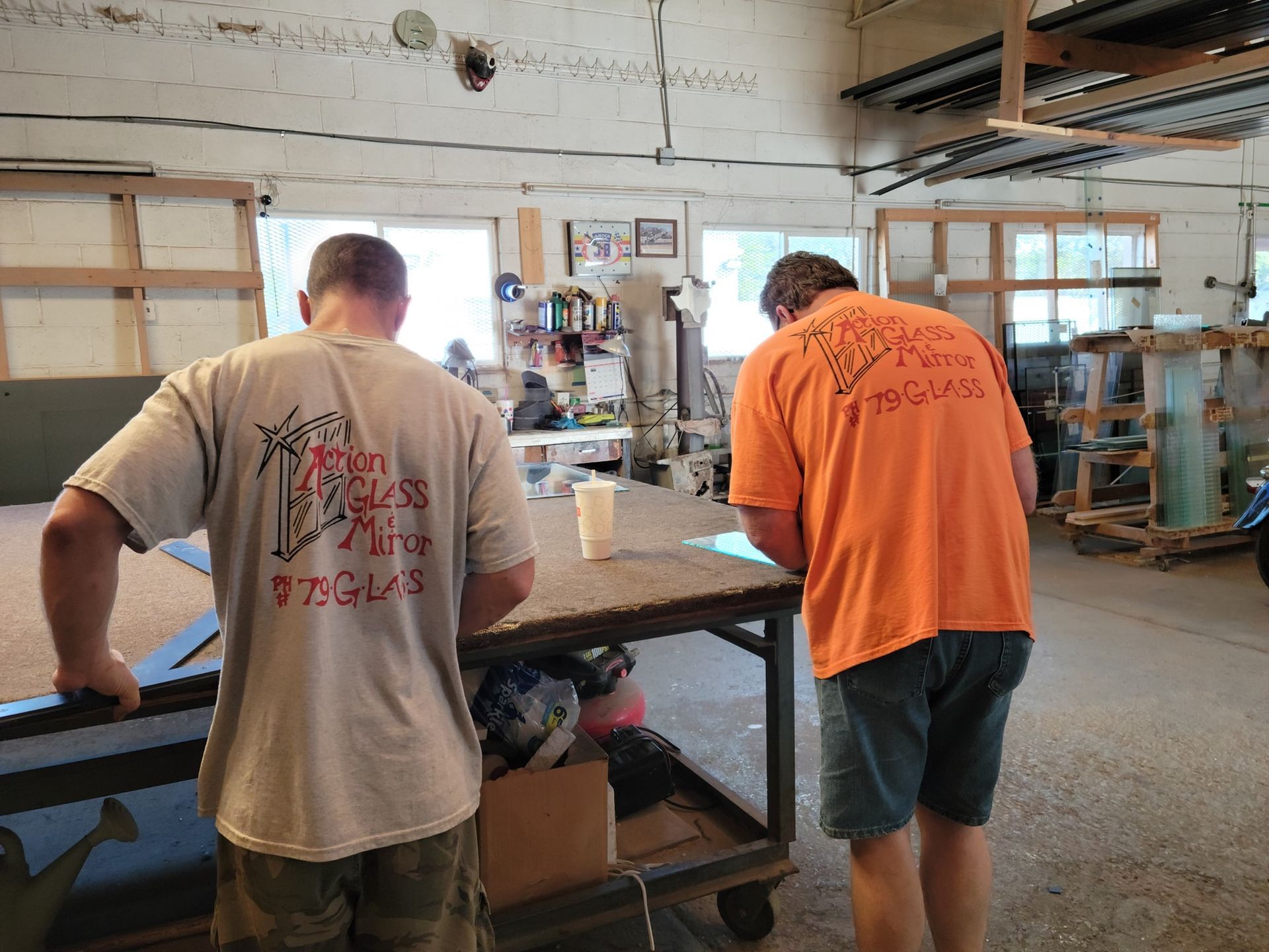 Two men in orange shirts are standing in a room looking at a table.