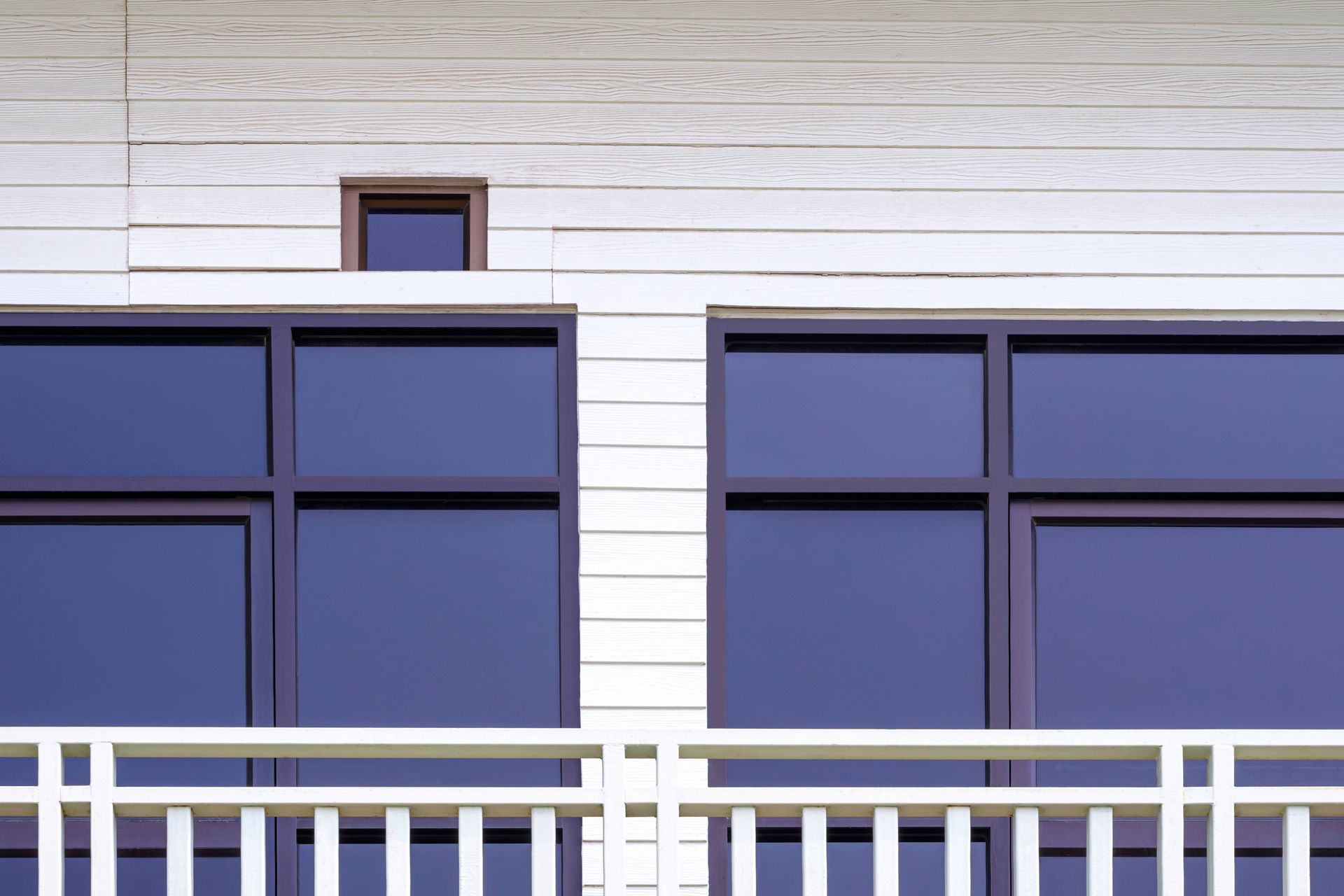 A balcony on the side of a building with blue windows and a white railing.