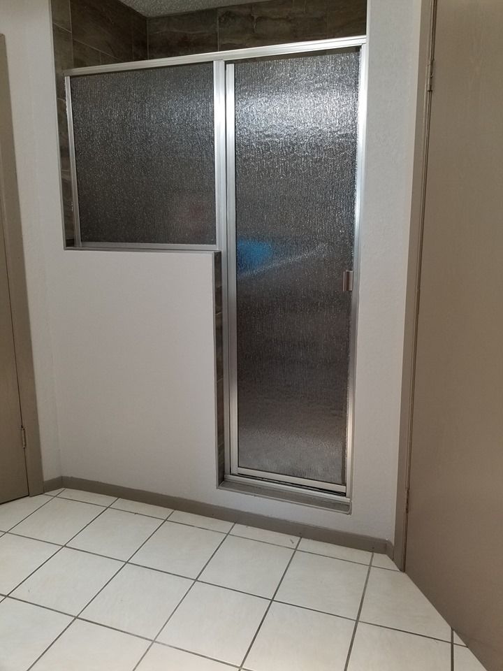 A bathroom with a glass shower door and a tiled floor.