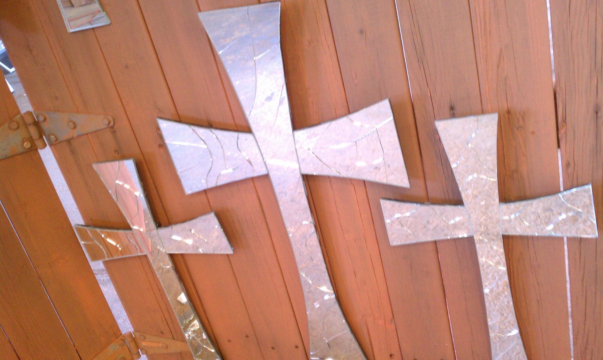 Three metal crosses are hanging on a wooden wall