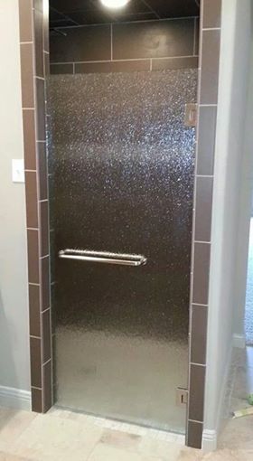 A bathroom with a glass shower door and a stainless steel handle.