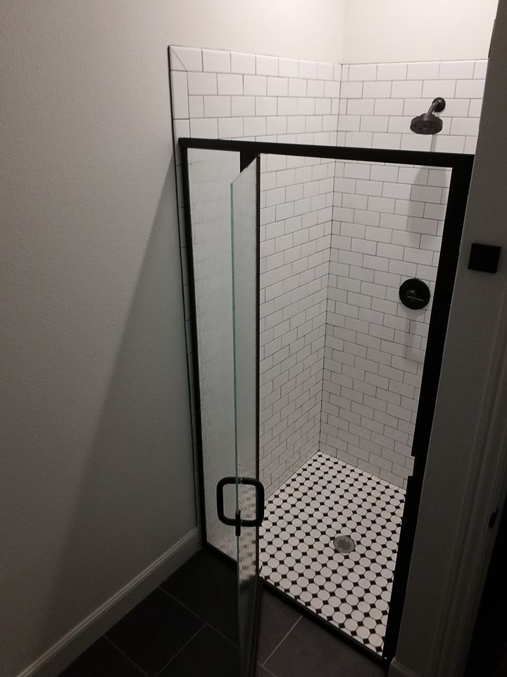 A shower with a black frame and white tiles