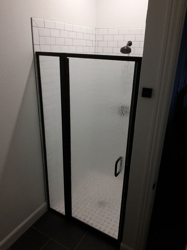 A shower stall with a black frame and a white tile floor.