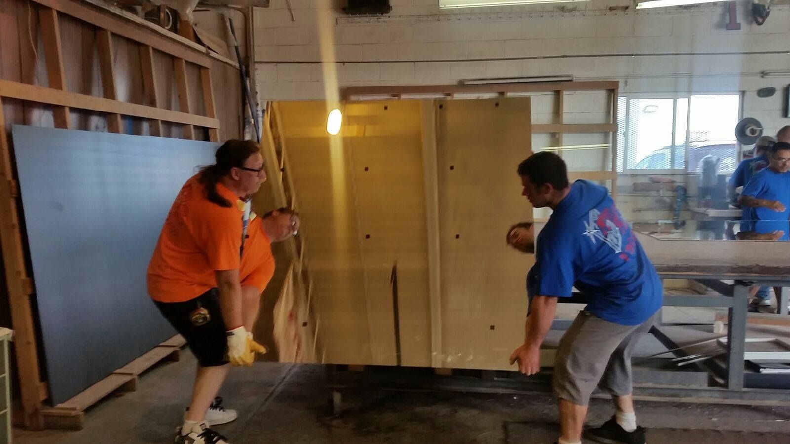 Two men in blue shirts are carrying a large wooden box