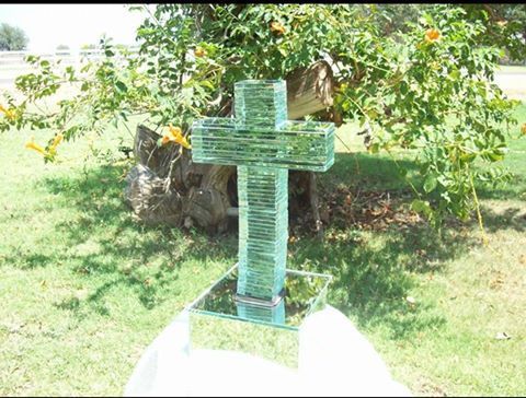 A glass cross is sitting in the grass in front of a tree