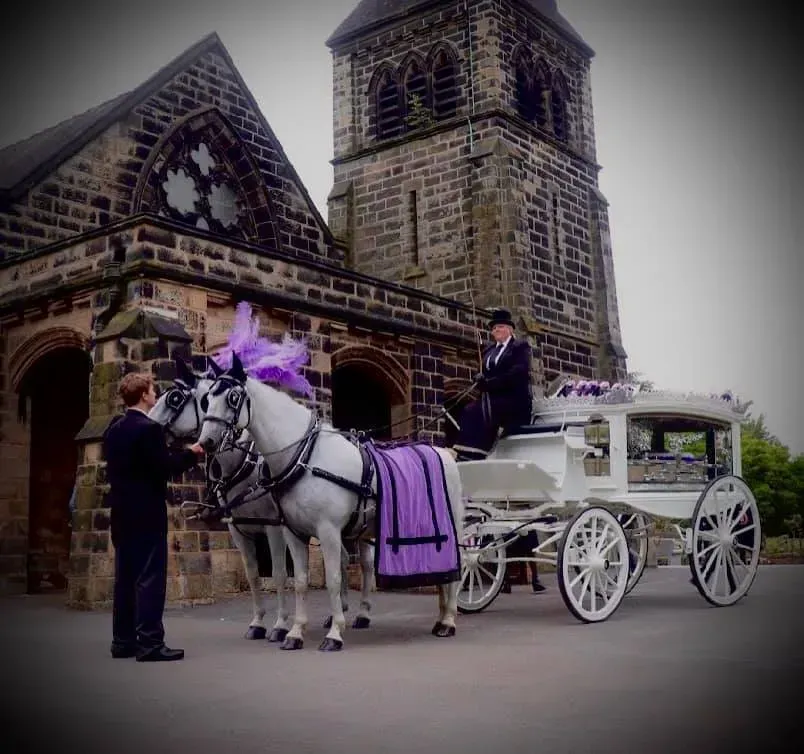 A man sits on a horse drawn carriage in front of a church
