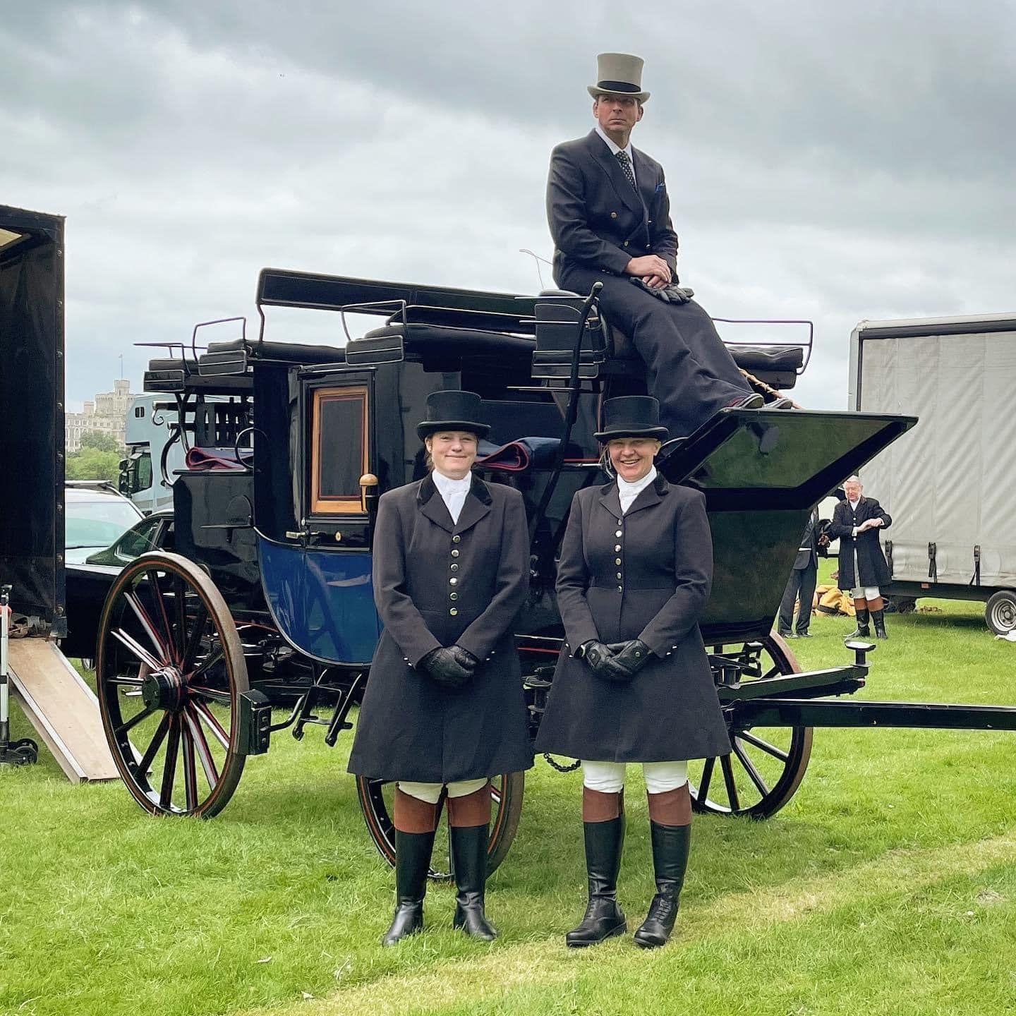 A man in a top hat sits on the back of a horse drawn carriage