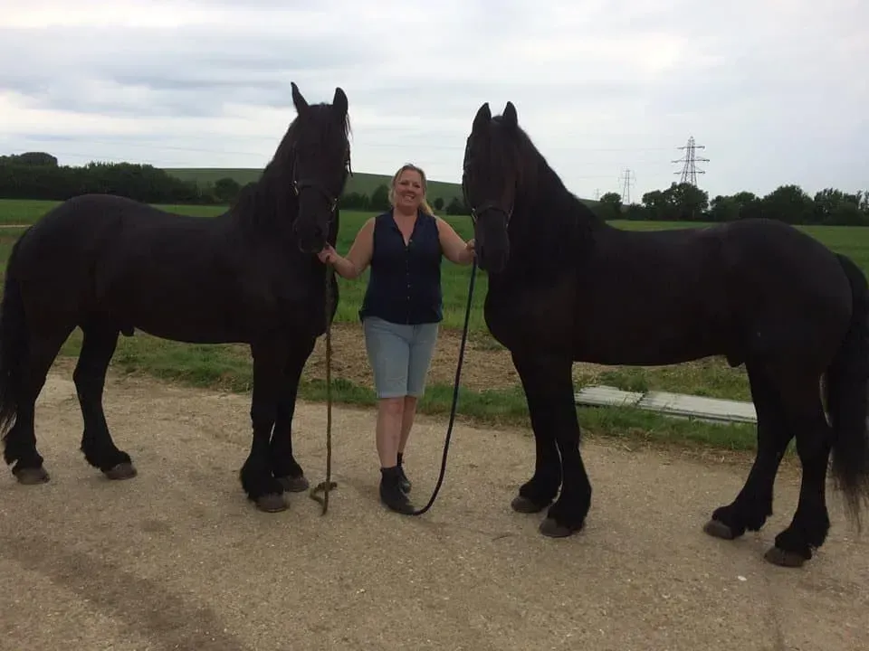 A woman standing next to two black horses on a dirt road