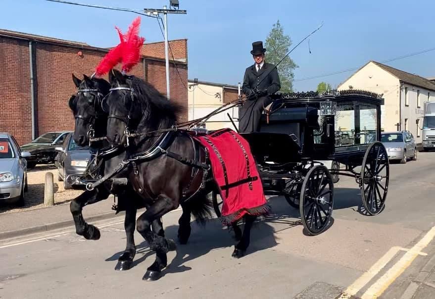 A man in a top hat is driving a horse drawn carriage down a street.