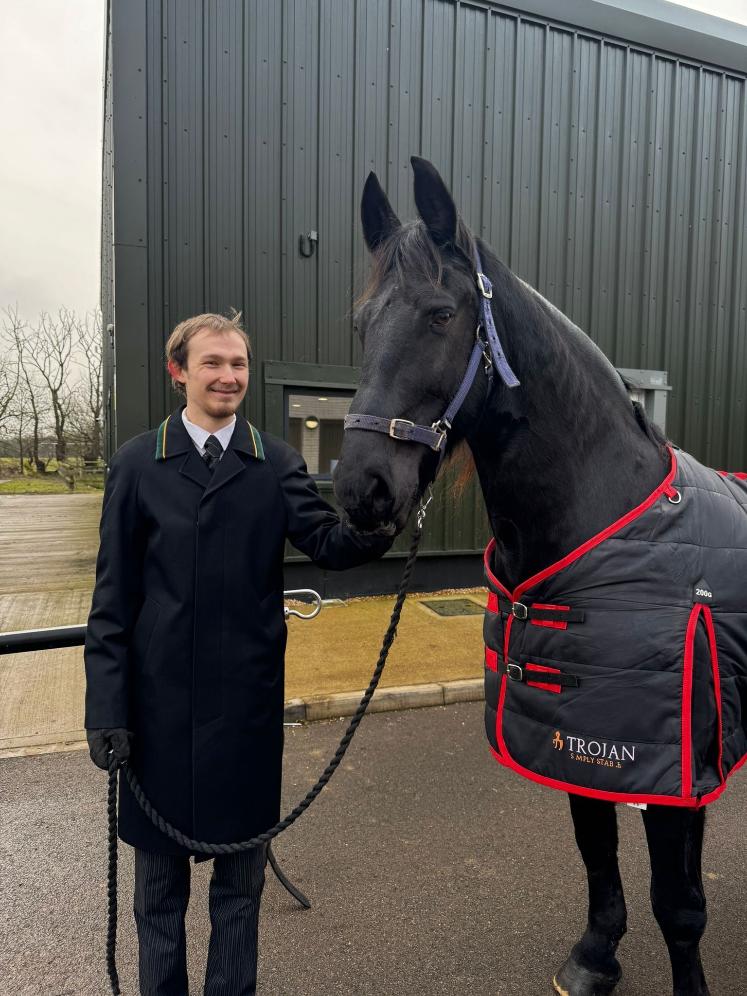 A man standing next to a black horse with a black blanket on it