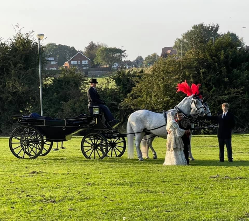 A bride and groom are standing next to a horse drawn carriage