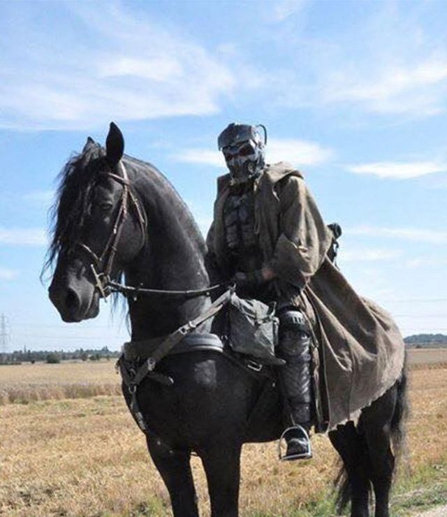 A man wearing a gas mask is riding a black horse