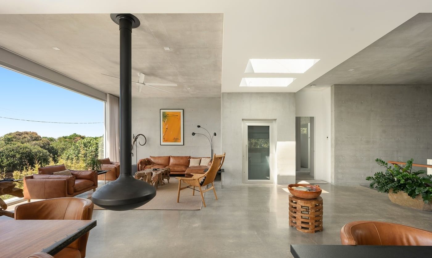 A modern, minimalist living room with concrete walls, a suspended black fireplace, leather seating, and a large window — SC Glass & Aluminium in Yandina, QLD
