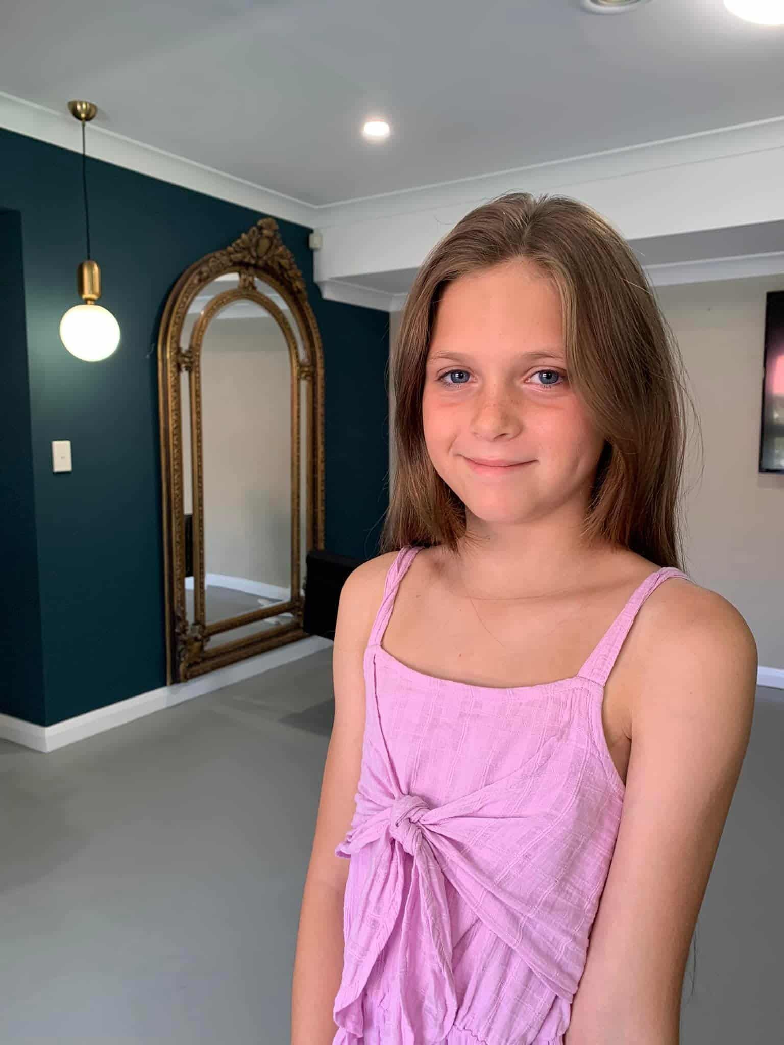 A Young Girl In A Pink Dress Is Standing In Front Of A Large Mirror In A Room — Minnie & Lucille Hairdressing In Armidale, NSW