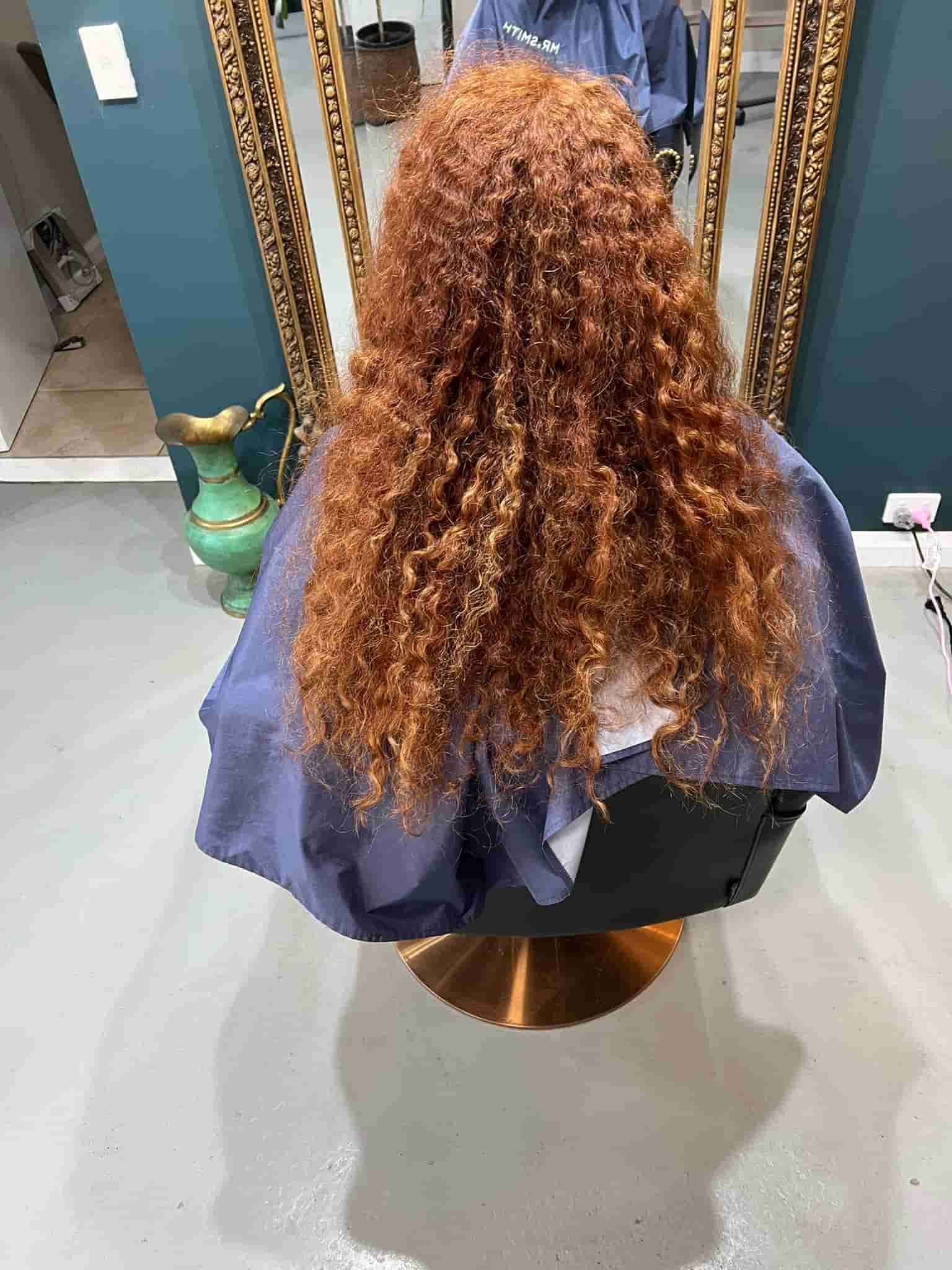 A Woman With Red Curly Hair Is Sitting In A Chair In Front Of A Mirror— Minnie & Lucille Hairdressing In Armidale, NSW 