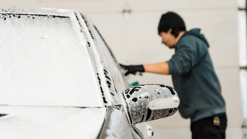 Person washing a car covered in white foam.