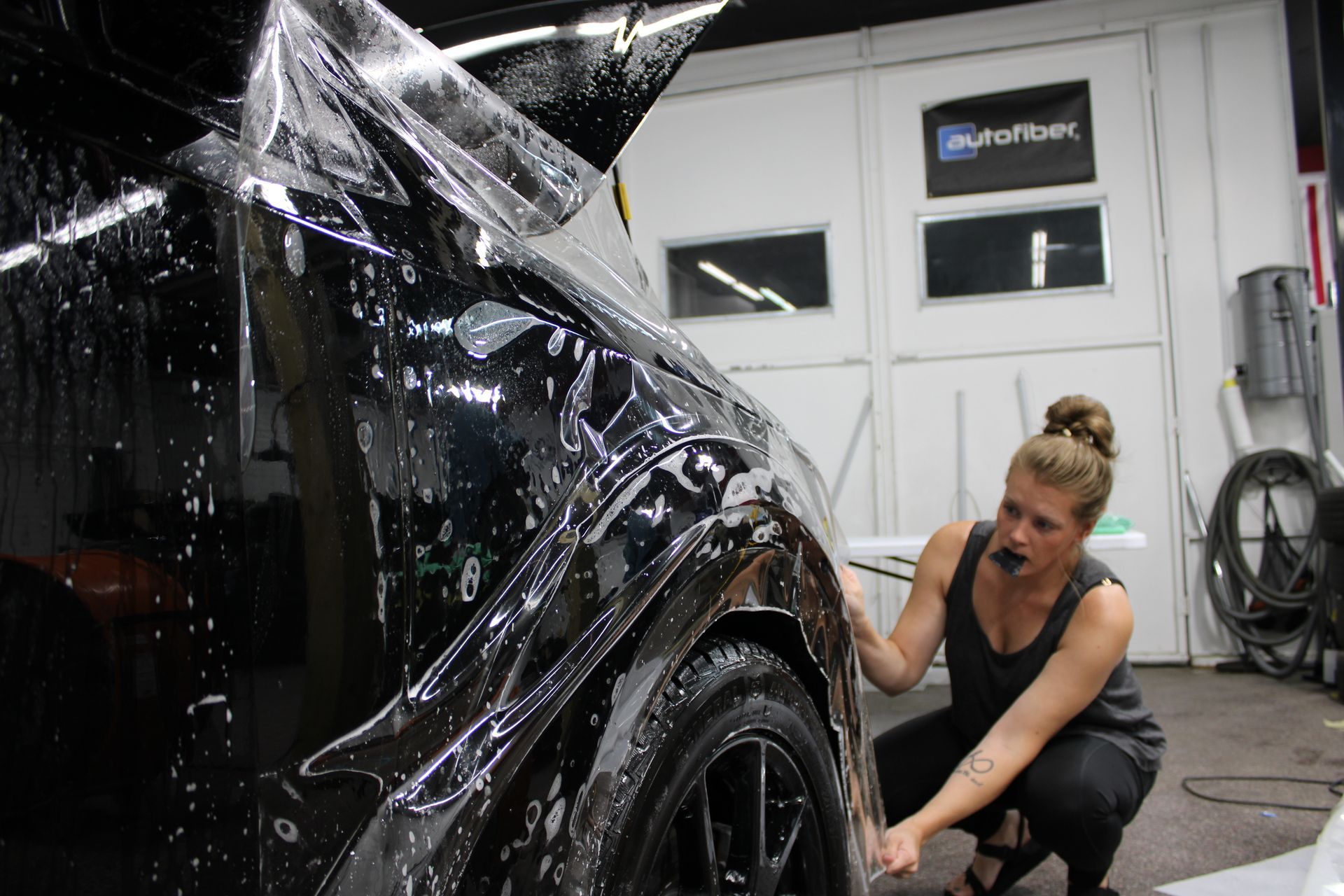 Woman applying protective film to a black car in a garage.