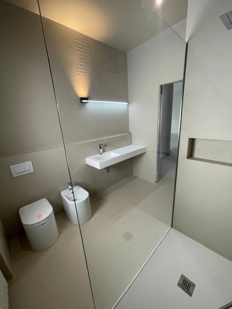 Bagno moderno con pareti beige, sanitari bianchi (lavandino, WC, bidet) e doccia in vetro.