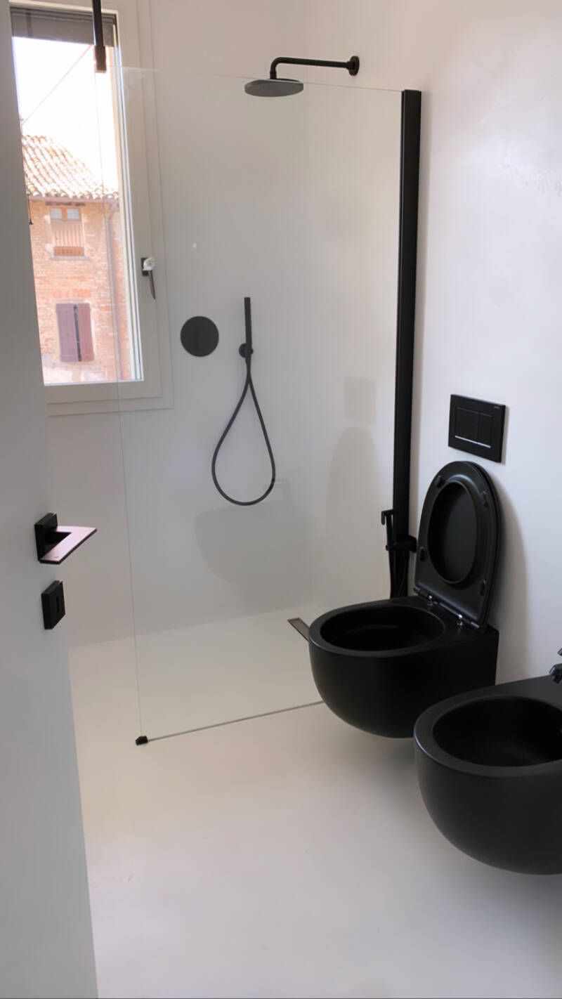 Bagno moderno con pareti bianche, WC e bidet neri, doccia e finestra.